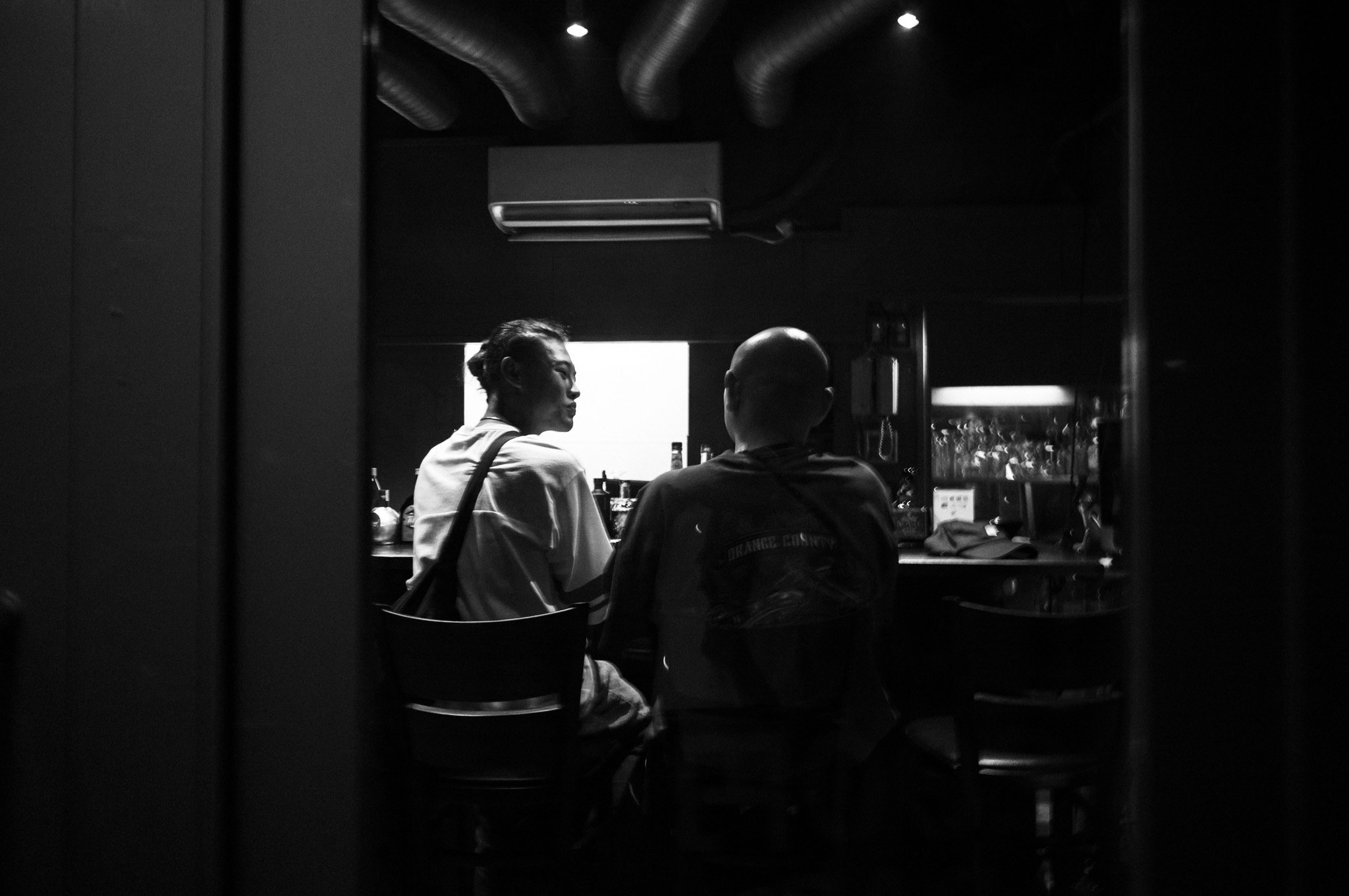 Two backs at a counter, and the window keeps their secret.