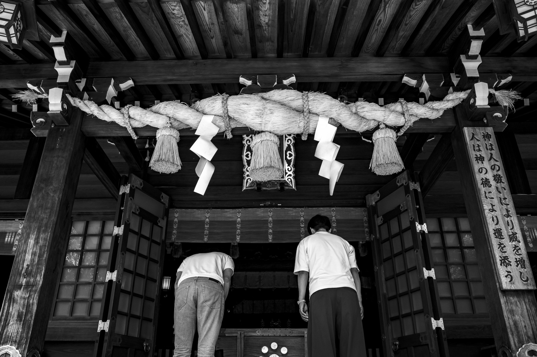 Two people bow before a shrine under a thick sacred rope.