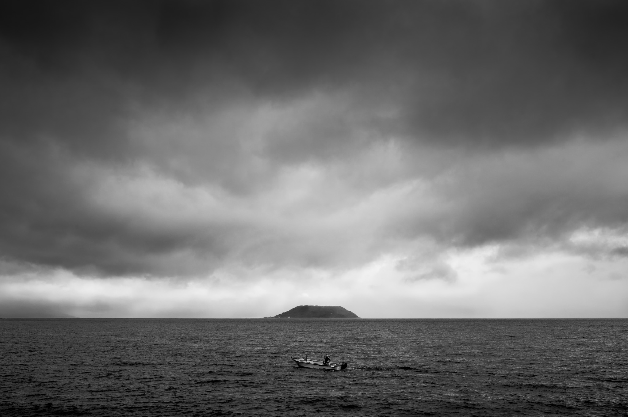 A small boat on a dark sea beneath heavy clouds, an island on the horizon.